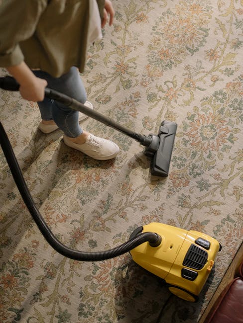 Three professional cleaners from Rush Green Carpet Cleaners are engaged in surface cleaning inside a modern living room. The room features a large L-shaped fabric sofa situated against a white wall wi